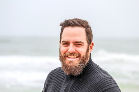 Man Wearing Black Zip-up Jacket Near Beach Smiling At The Photo photo