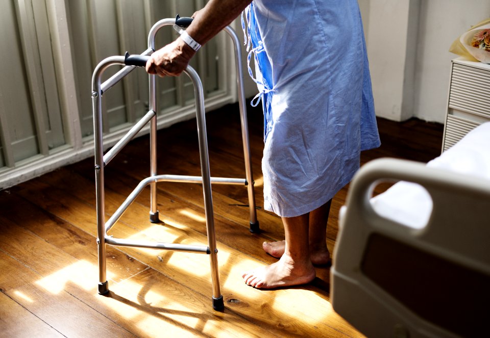 Person In Hospital Gown Using Walking Frame Beside Hospital Bed