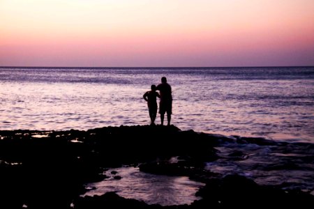 Father And Child Near On Body Of Water During Sunset photo
