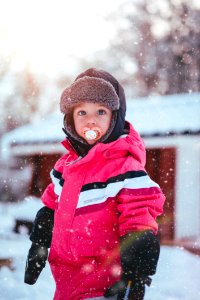 Toddler Boy Wearing Red And Black Winter Jacket And Gray Ushanka Hat Standing On Snow Covered Field photo