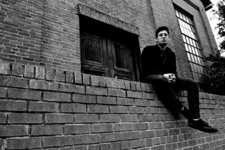 Grayscale Photography Of Man Sitting On Brick Fence photo