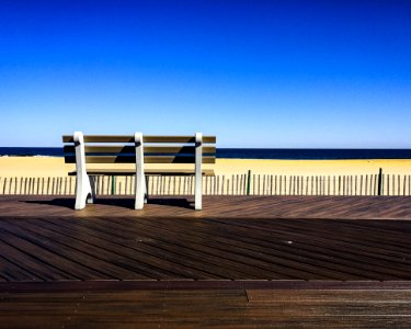 Brown-and-white Wooden Bench Facing Body Of Water Under Clear Blue Sky photo