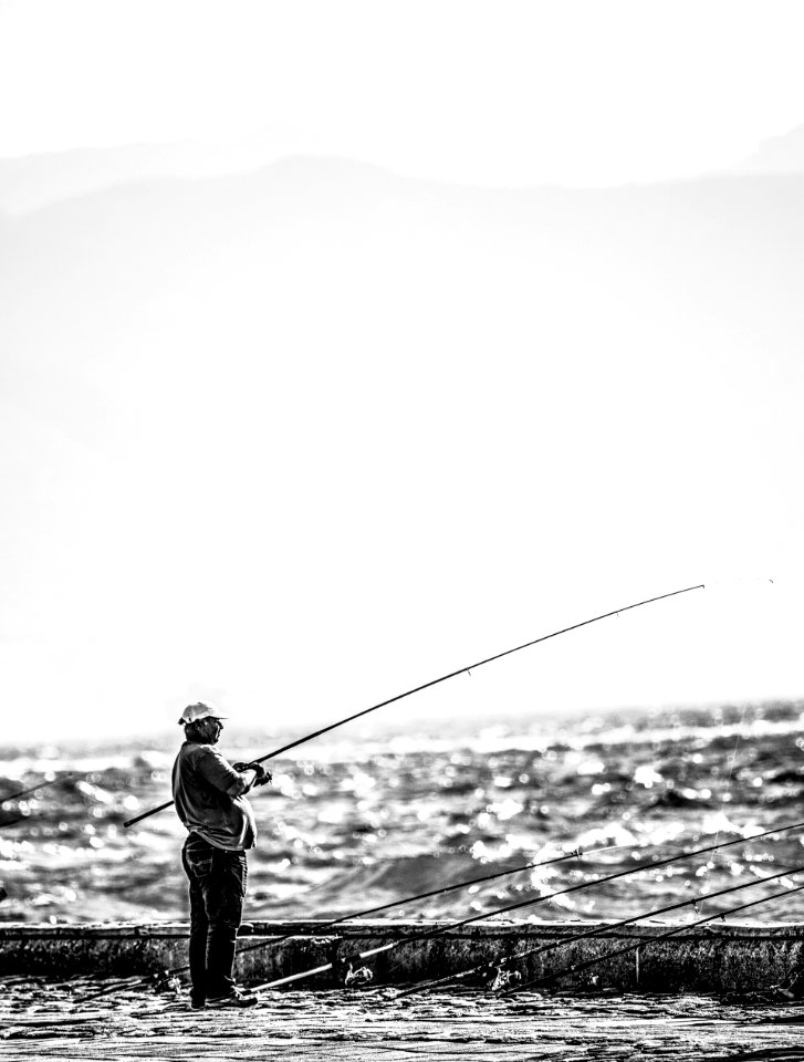 Man Standing Near Seashore Holding Fishing Rod On Grayscale Photography