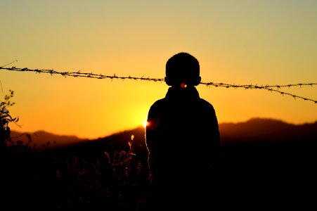 Silhouette Of Boy Standing Near Barbed Wire Fence During Golden Hour photo