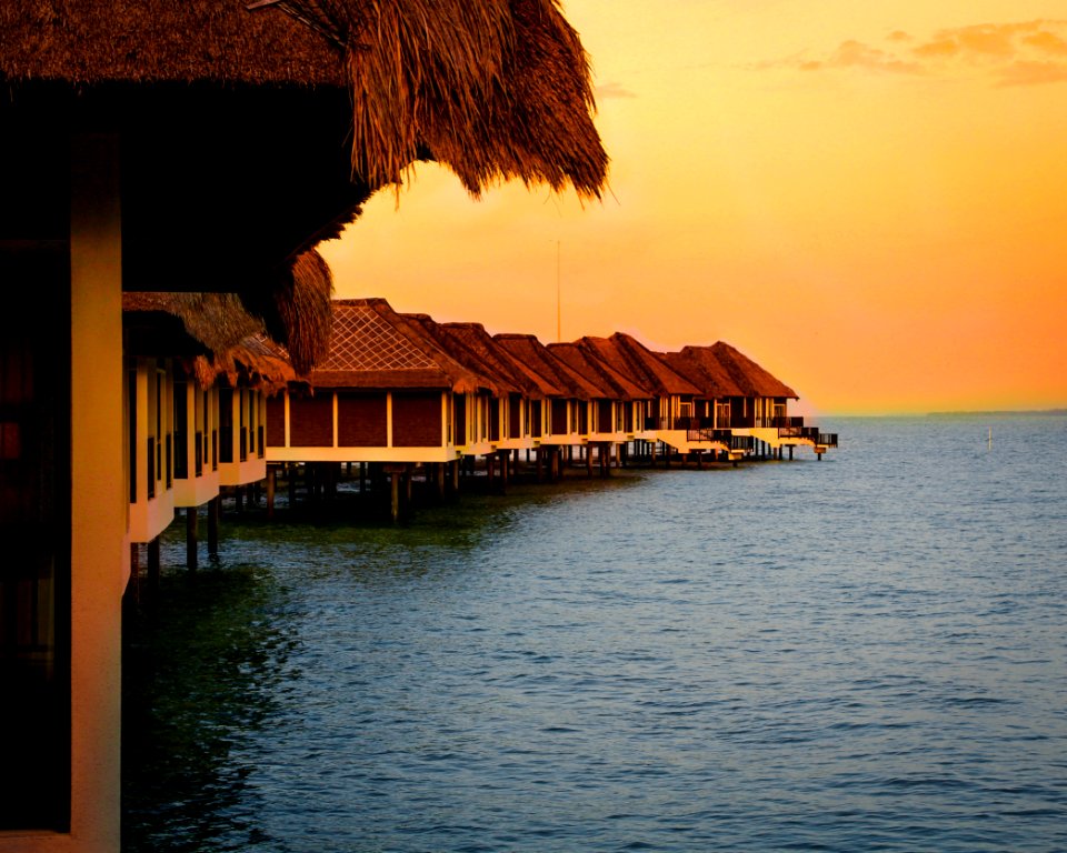 Architectural Photography Of Brown Stilt Houses On Top Of Sea Under Orange Sky