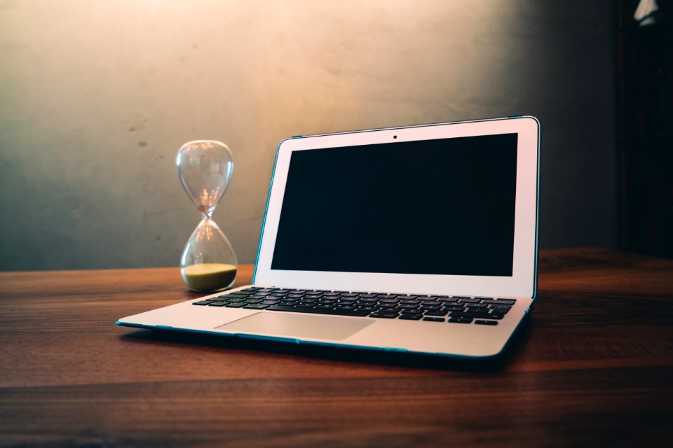 Computer Laptop Beside Hour Glass On Brown Wooden Surface