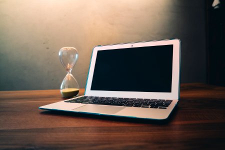 Computer Laptop Beside Hour Glass On Brown Wooden Surface photo