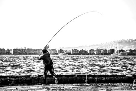 Grayscale Photography Of Man Holding A Fishing Rod Near Body Of Water photo