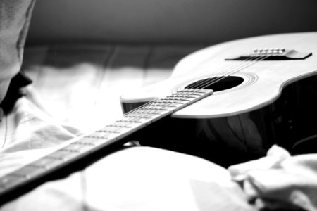 Gray Scale Photography Of Acoustic Guitar On Bed photo