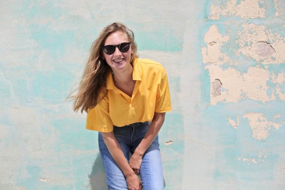 Woman Wearing Yellow Polo Shirt Standing In Front Of Teal Concrete Wall