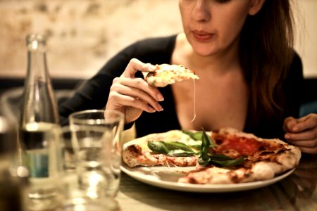 Woman Holds Sliced Pizza Seats By Table With Glass photo