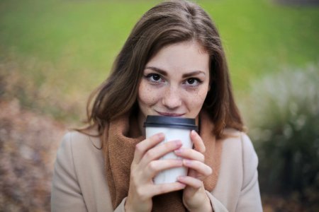 Woman In Brown Top And Scarf Holding A White And Black Travel Cup Outside photo