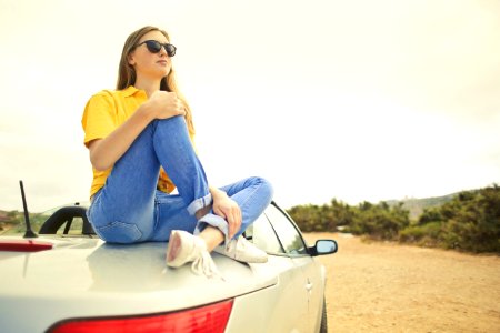 Woman Wears Yellow Shirt And Blue Denim Jeans Sits On Silver Car photo