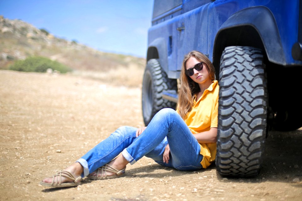 Woman In Yellow Polo Shirt Sitting On Ground Leaning On Blue Vehicle At Daytime photo