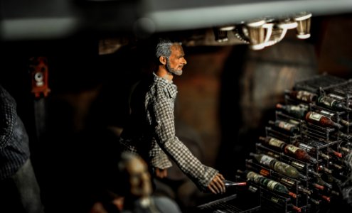 Selective Focus Photography Of Male Doll Holding Bottle Near Bottle Rack