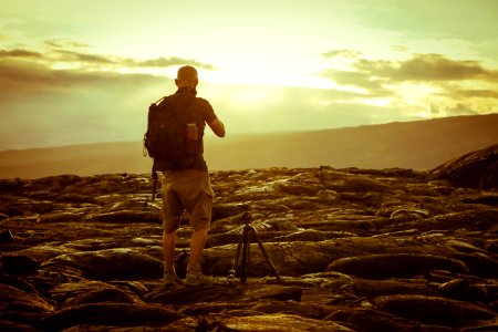 Man Beside Tripod On Rocks During Golden Hour photo