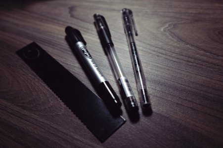 Three Ballpoint Pens And Black Ruler On Beige Wooden Surface photo