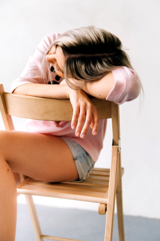 Woman Wearing Pink Long Sleeve Shirt And Blue Denim Short Shorts Sitting On Brown Wooden Folding Chair