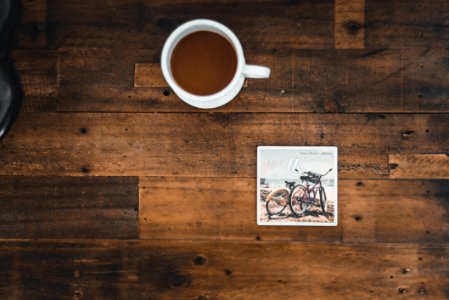 White Ceramic Mug With Coffee Beside Photo Of Two Mountain Bikes