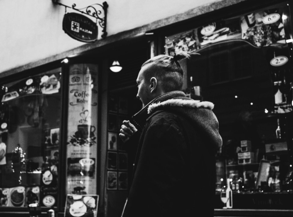 Grayscale Photograph Of Man Walking Past By Shop