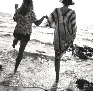 Grayscale Photograph Of 2 Women Holding Hands While Walking On Sea Shore photo