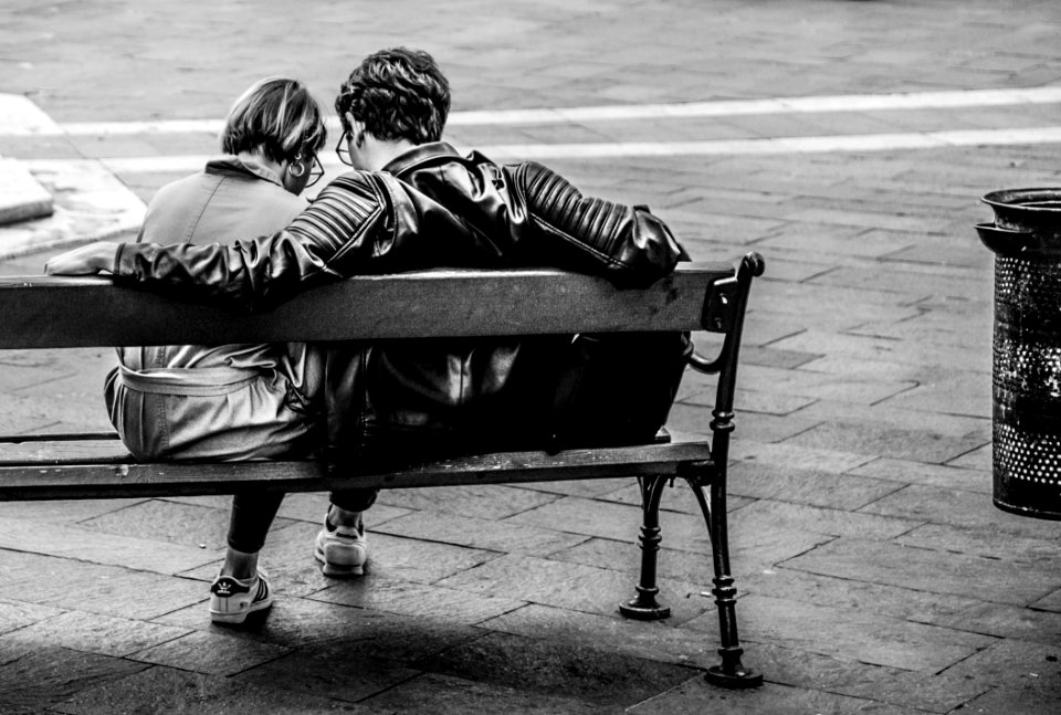 Grayscale Photo Of Two Person Sitting On A Bench