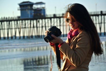 Selective Focus Photography Of Woman Holding Her Camera Near Seashore photo