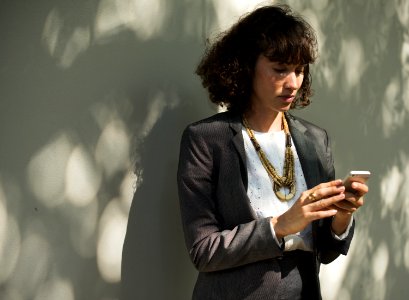 Woman In Black Blazer Holding A Smartphone While Standing Near Wall photo