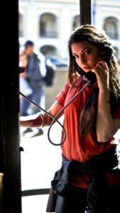 Woman In Red T-shirt Holding Telephone Inside Telephone Booth