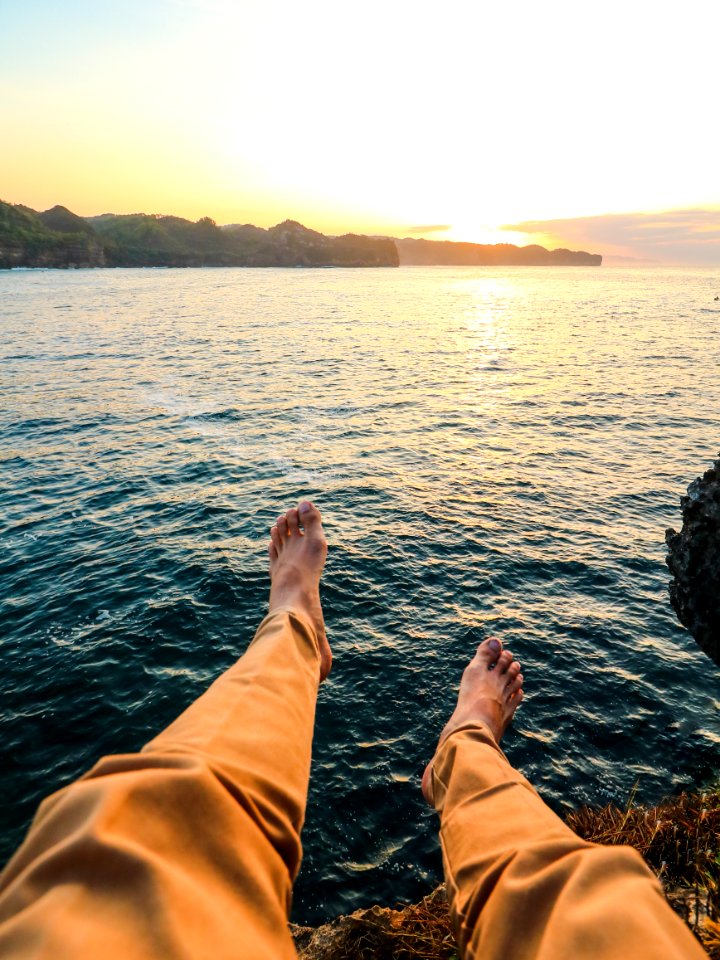 Person Wearing Yellow Pants Sitting On Rock Surrounded By Sea