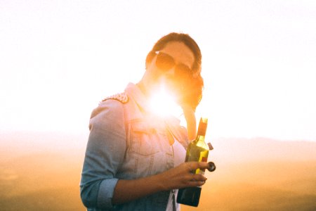 Woman Wearing Blue Denim Jacket Holding Wine Bottle In Golden Hour Photo photo