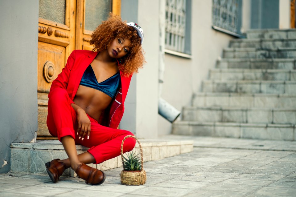 Woman Wearing Red Coat And Pants Sitting Outside Gray Building