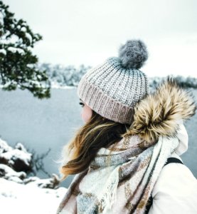 Woman In White And Brown Parka Jacket Wearing Grey Knitted Bobble Hat Near Blue Sea Under White Sky photo