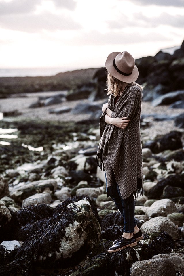 Woman Wearing Draped Coat Standing On Rock Facing Mountain