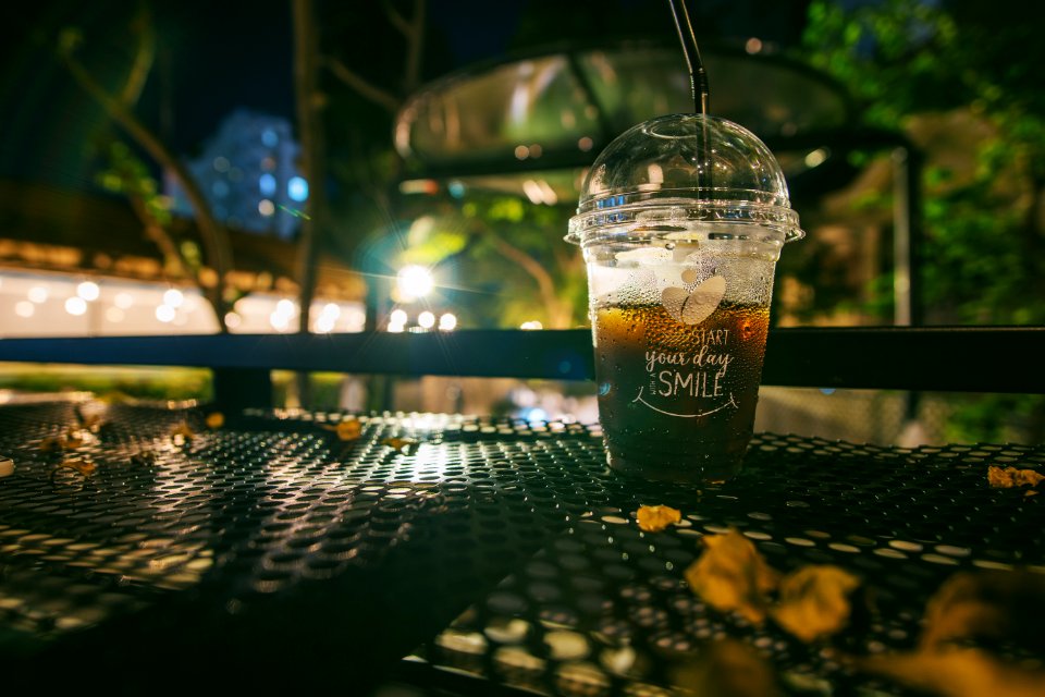 Clear Plastic Disposable Cup With Straw Half-filled With Juice On Metal Table photo