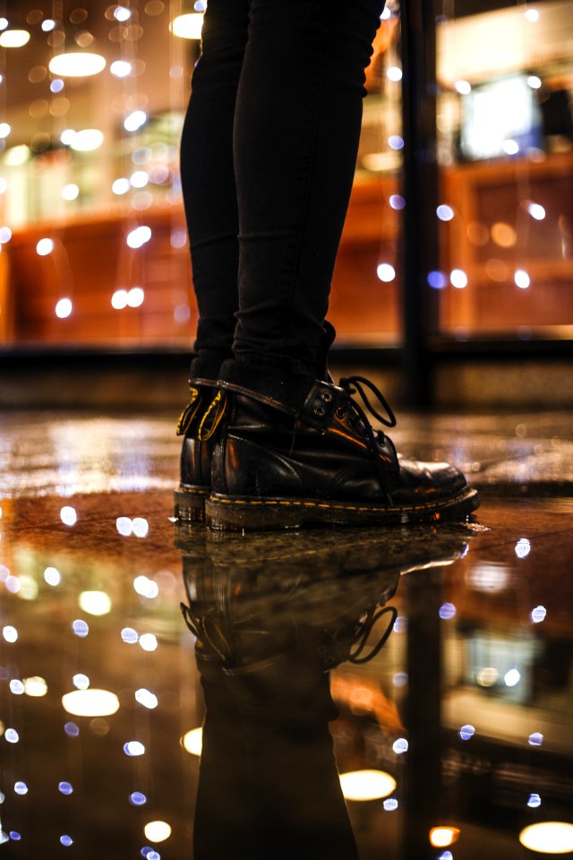 Photo Of Person Wearing Black Fitted Jeans And Black Drmartens Boots Standing On Black Floor Tiles