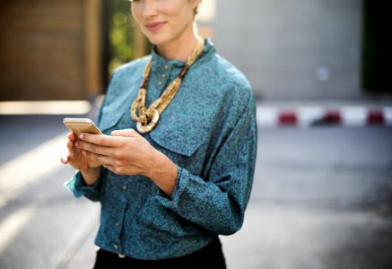 Woman Holding Iphone Wearing Long-sleeved Shirt And Gold Necklace photo