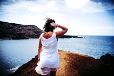 Woman Wearing White Sleeveless Mini Dress On Top Of Brown Sand Near Body Of Water photo