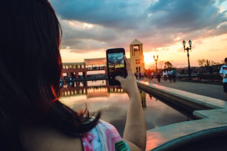 Woman Holding Smartphone Capturing Sunset photo