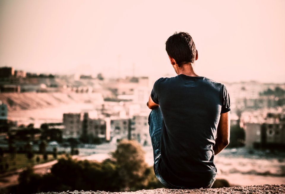 Man In Black Shirt And Blue Denim Jeans Sitting On Gray Stone At Daytime