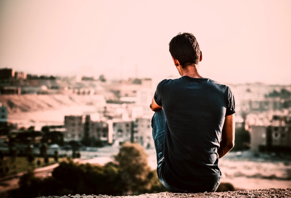 Man In Black Shirt And Blue Denim Jeans Sitting On Gray Stone At Daytime photo