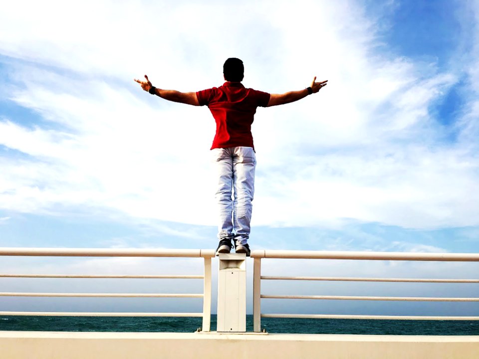 Person Raising Hands Mid-air Sidewards While Standing On Gray Steel Railings