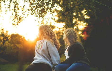 Two Women Sitting Near Green Tree During Sunset