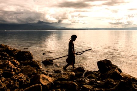 Person Holding Spear Beside Body Of Water photo