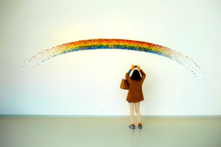 Woman Wearing Brown Top And Beige Leggings Taking Picture Rainbow Painted Wall