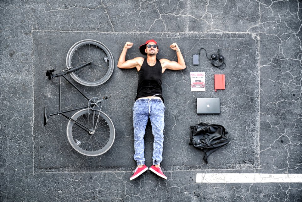 Man In Black Tank Top Laying On Gray Concrete Surface Near Black Bike