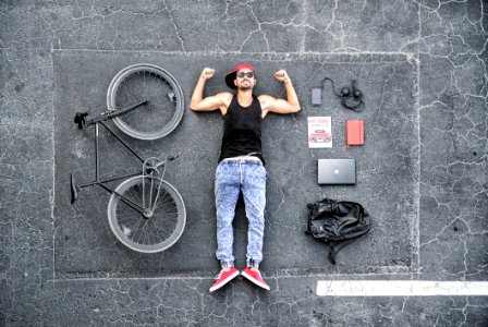 Man In Black Tank Top Laying On Gray Concrete Surface Near Black Bike photo