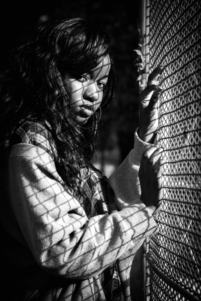 Grey Scale Photography Of Woman Standing Against Mesh Grill