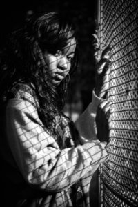 Grey Scale Photography Of Woman Standing Against Mesh Grill photo