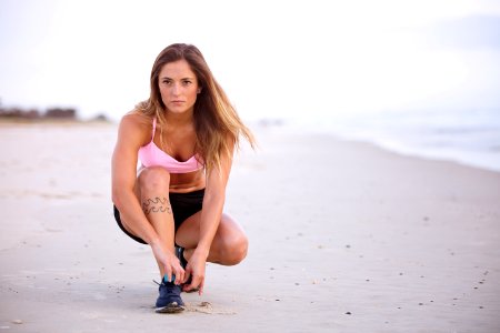 Woman In Pink Top And Black Shorts Lacing Her Shoes On Sea Shore